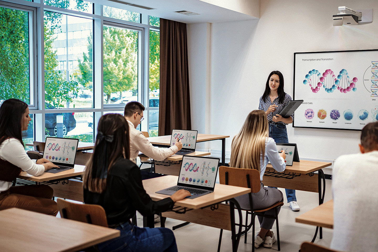 A classroom of students using Samsung laptops at their desks while a teacher lectures at the front.