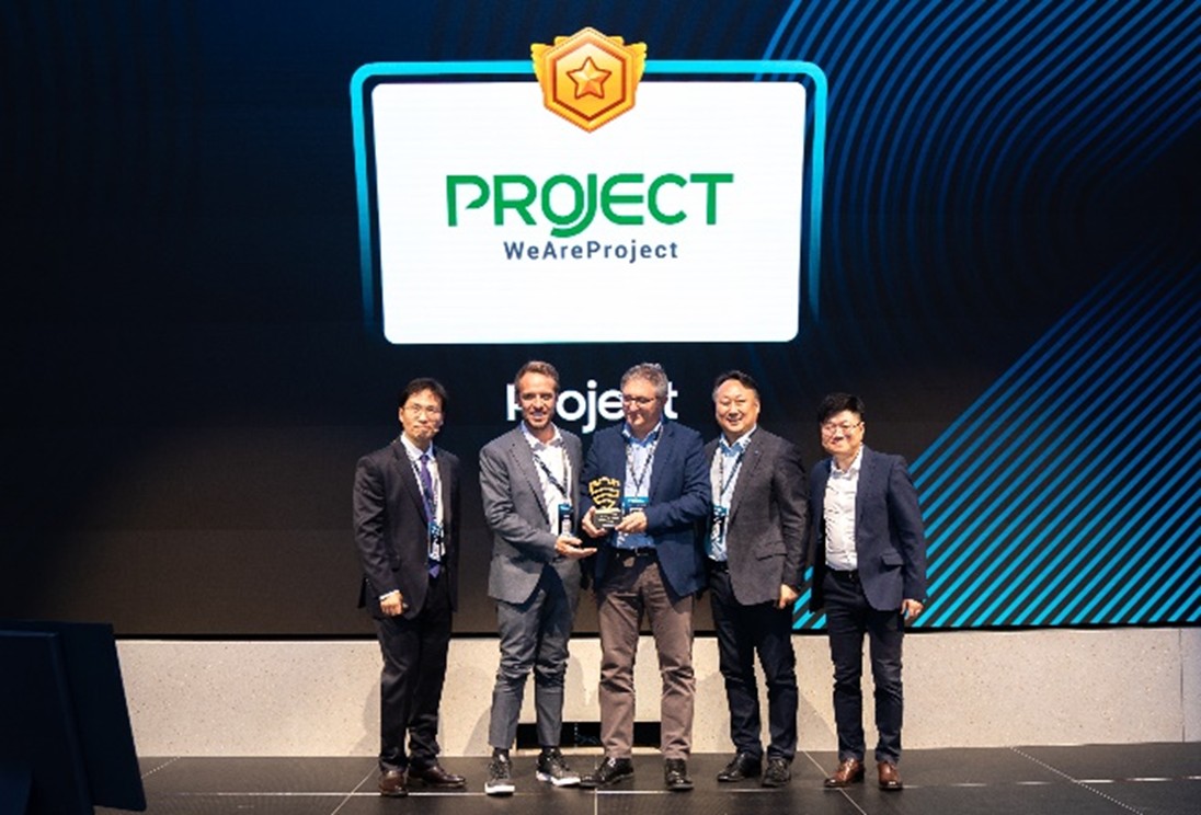 A group of five men standing on stage holding an award trophy, with a large screen behind them displaying the text 'PROJECT - WeAreProject.'