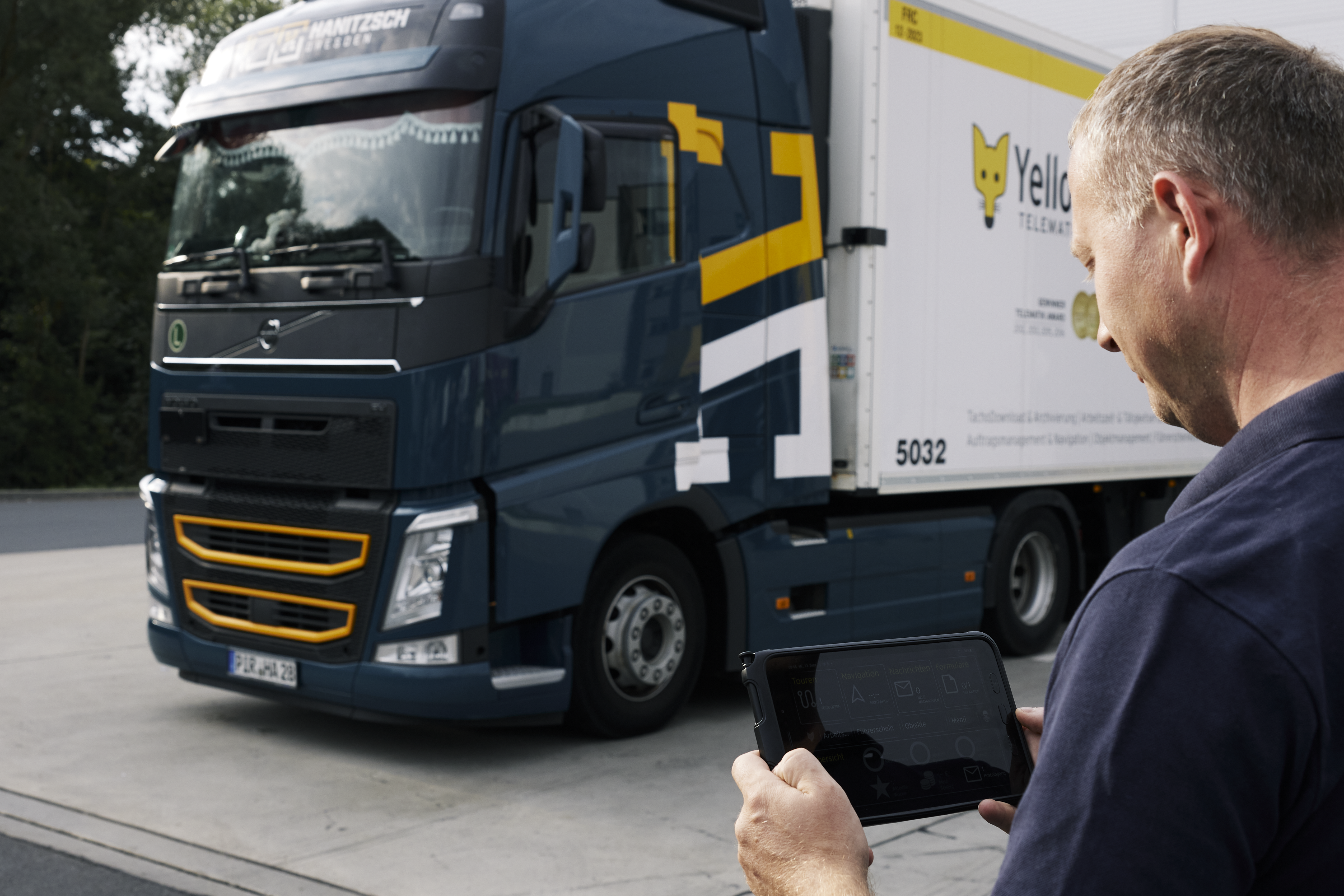 A picture of a YellowFox employee looking at their Samsung tablet device, with a YellowFox truck parked in a lot in the background.