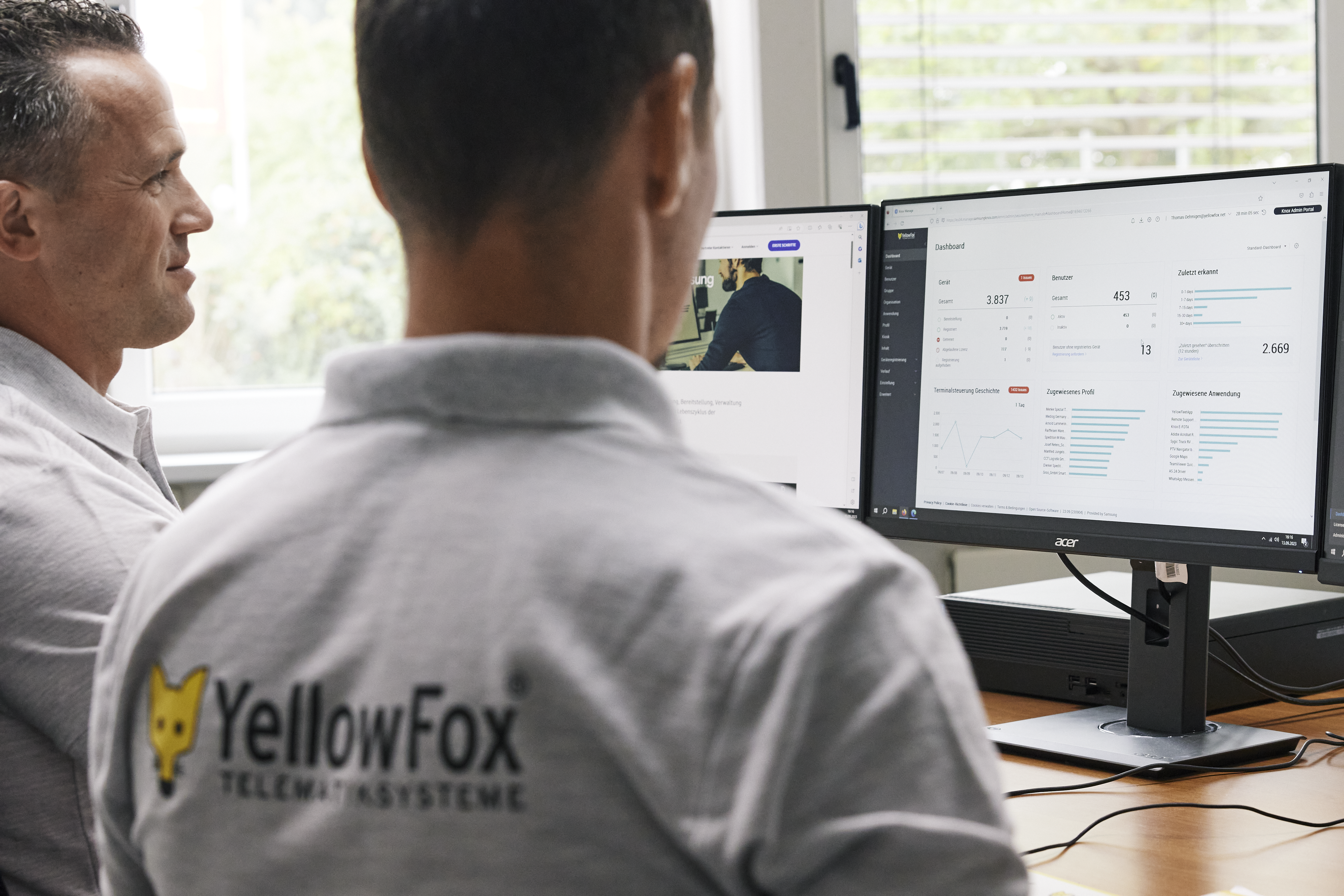 Two YellowFox employees sitting in front of a double-monitor setup while viewing the Knox Admin Portal dashboard.
